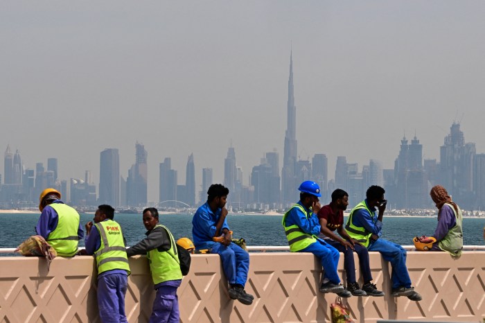 سقوط آرامش دبی؛ چگونه جنگ ایران تصویر لوکس خلیج فارس را بر هم زد؟ Workers resting on a wall with the Dubai skyline and Burj Khalifa in the background.